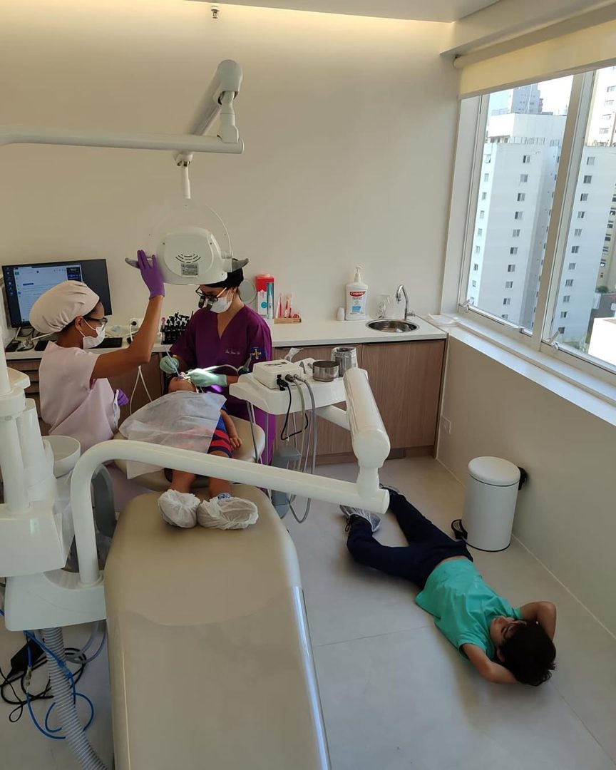 Equipe atendendo uma paciente na cadeira enquanto uma criança descansa deitada no chão da sala