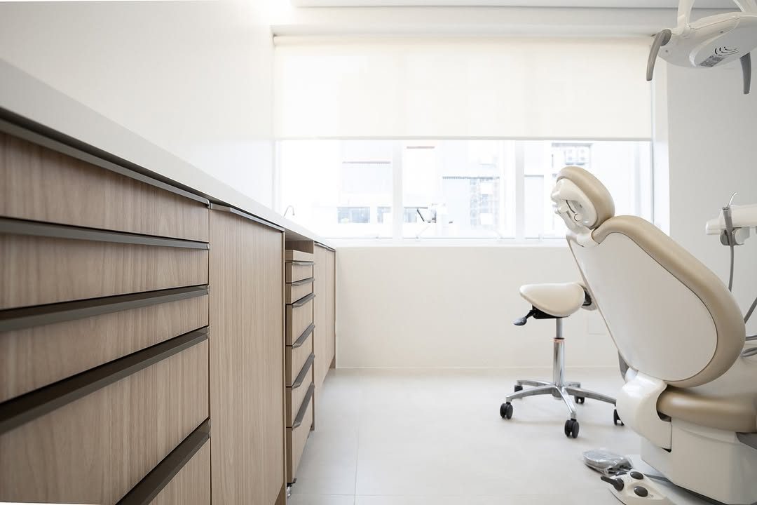Sala de atendimento clara com cadeira odontológica, armários de madeira e janela ampla