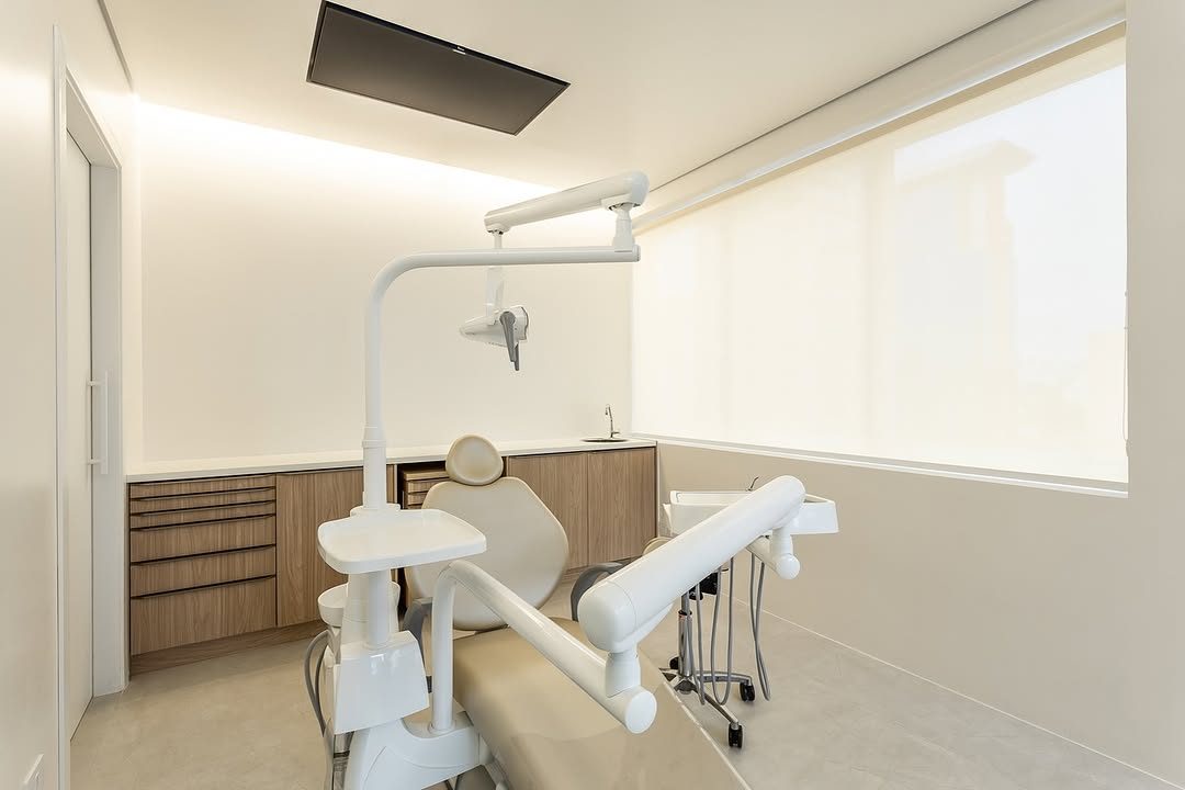 Sala de atendimento vista da porta, com cadeira odontológica, equipo e TV na parede