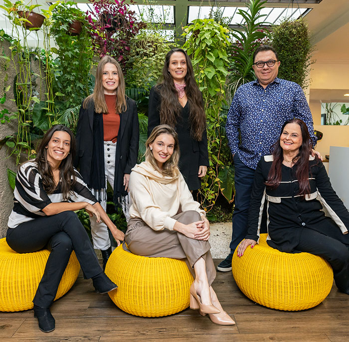 Dra. Joana Ozi e a equipe da clínica reunidas em um ambiente com plantas na clínica do Itaim Bibi